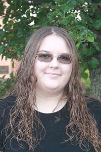 woman with light brown long wavy hair wearing a balck shirt and dark glasses